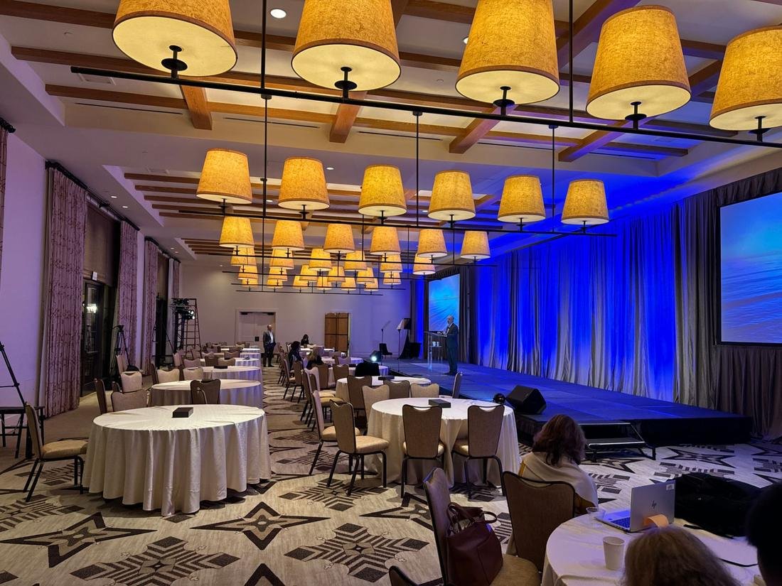 Event room with a stage and draped walls uplit in deep blue under large hanging lamps
