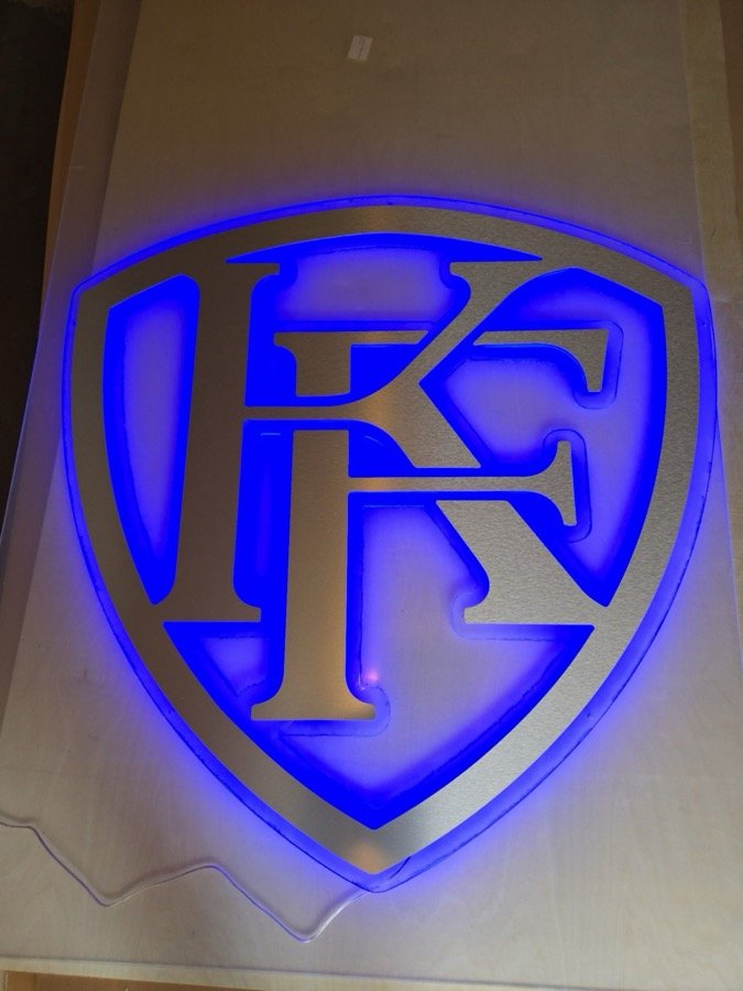 Brushed metal shield logo sign with a blue LED glow behind it