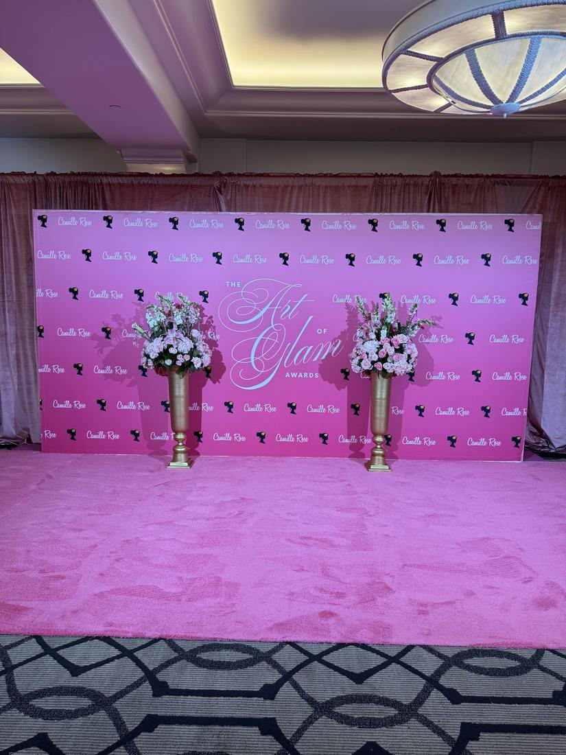 Pink step and repeat backdrop with tall gold vases of flowers on a pink carpet
